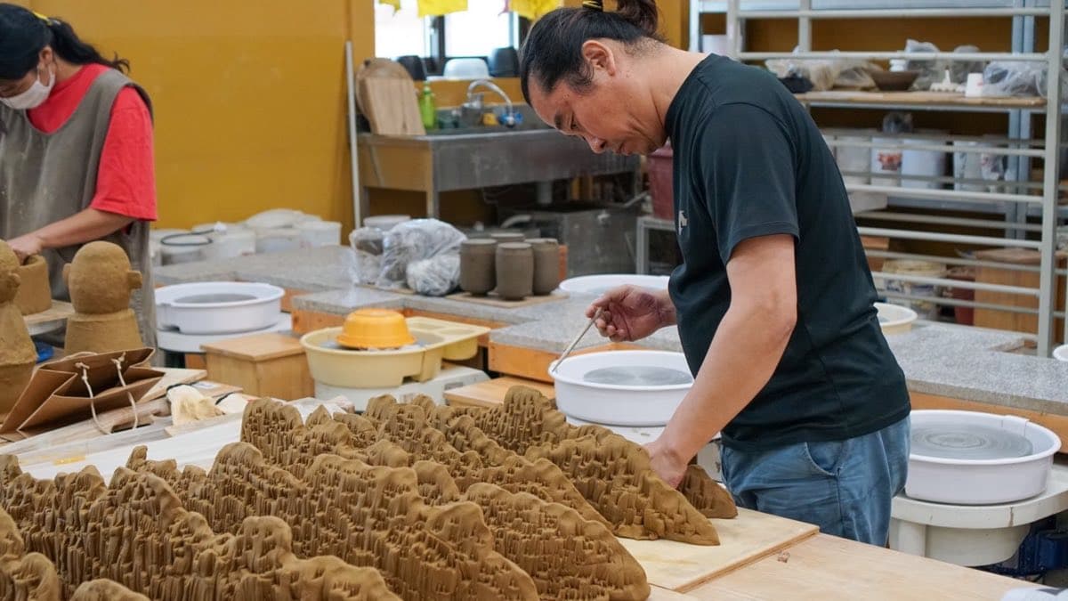 A tile artisan hand-shaping a Baekje ridge-end ornament in the workshop